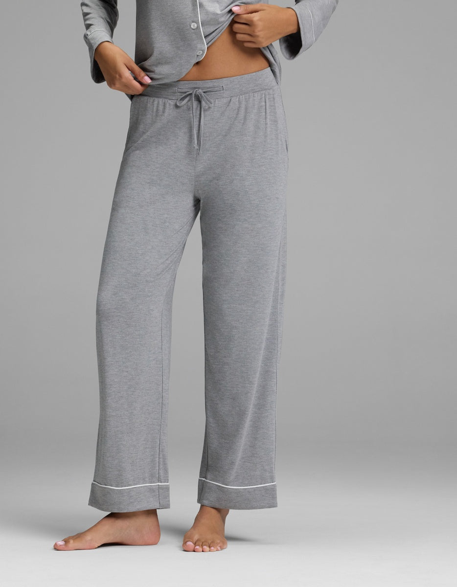 A person stands barefoot, wearing the Cozy Earth Women’s Bamboo Stretch-Knit Long Sleeve Pajama Set - Petite in light gray, featuring drawstring-waist pants with cuffed hems, paired with the matching long sleeve top. The image is cropped from the shoulders down against a plain background.
