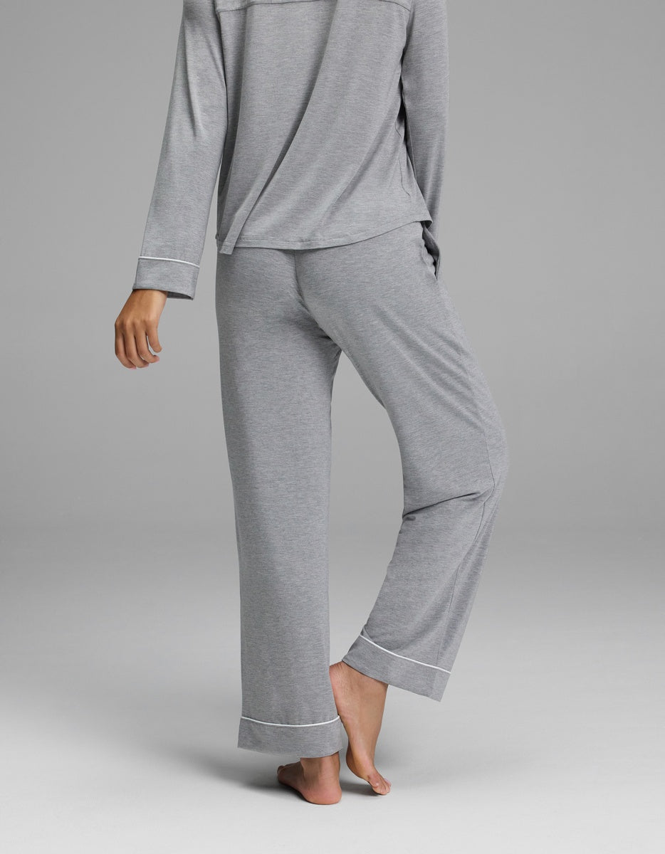A person is standing barefoot, seen from behind, wearing a matching light gray long-sleeve pajama top and Cozy Earth Women’s Bamboo Stretch-Knit Pajama Pant - Petite, against a plain gray background.