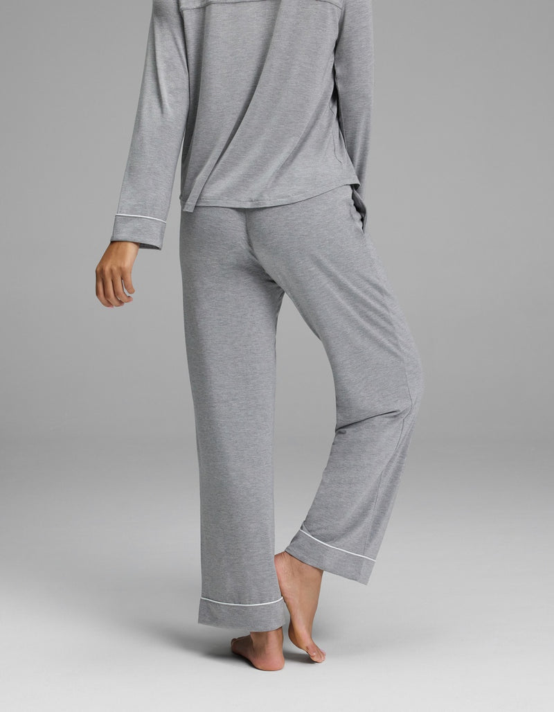 A person is standing barefoot, seen from behind, wearing a matching light gray long-sleeve pajama top and Cozy Earth Women’s Bamboo Stretch-Knit Pajama Pant - Petite, against a plain gray background.