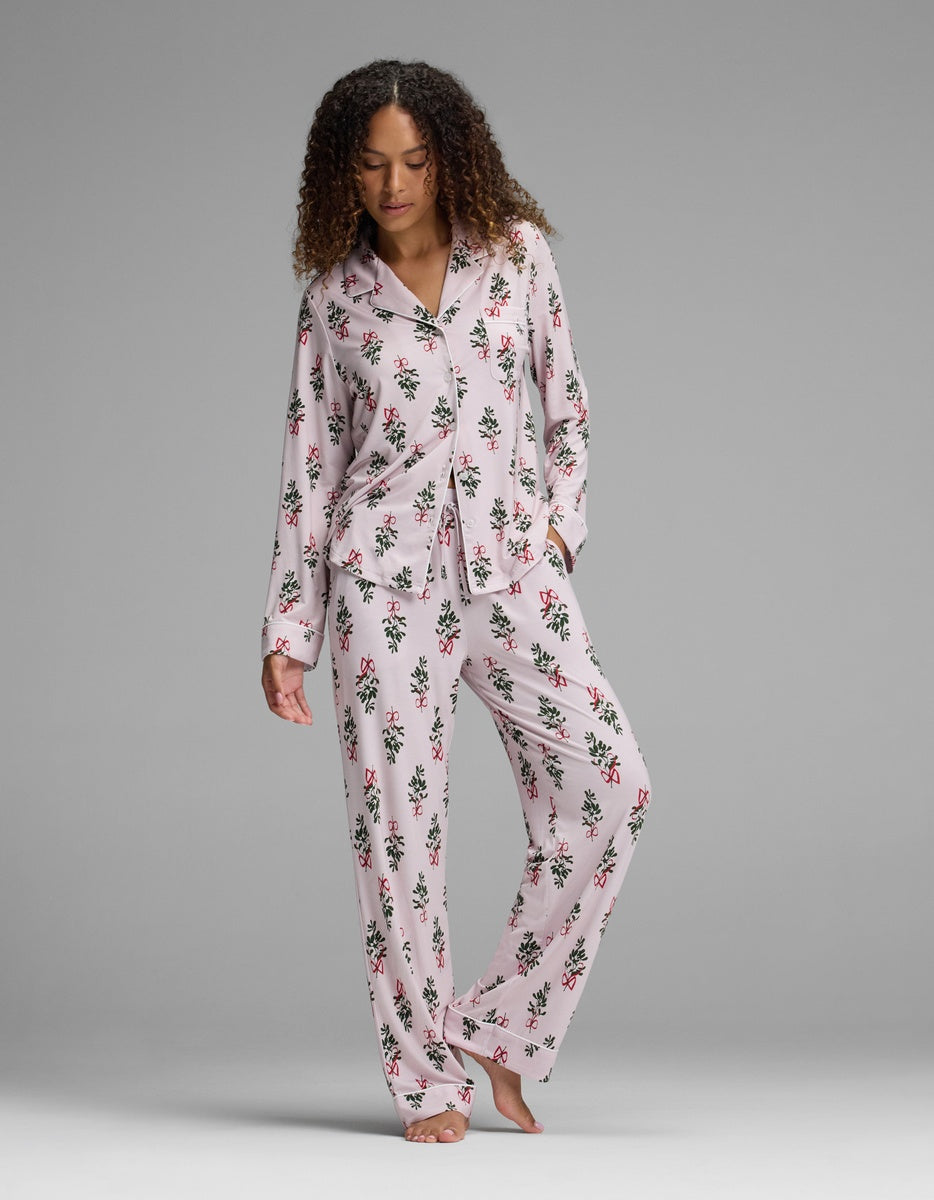 A person wearing a light pink Women’s Bamboo Stretch-Knit Pajama Pant set featuring a pattern of red bows and green holly sprigs.