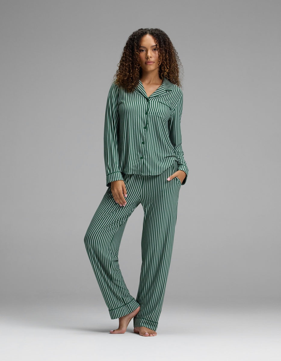 A person wearing a long-sleeved button-down pajama top and matching Women’s Bamboo Stretch-Knit Pajama Pant, both featuring dark green and black vertical stripes.