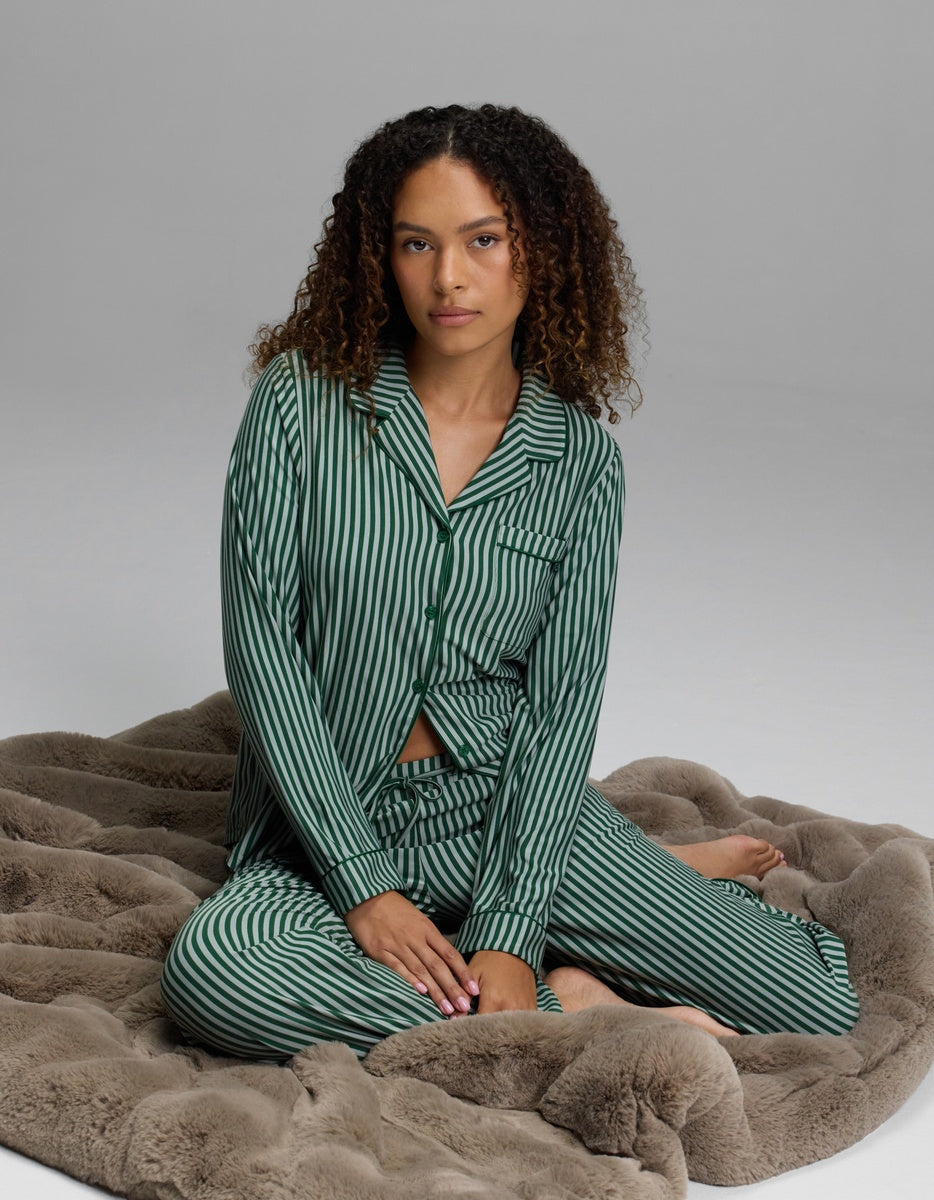 A person wearing a dark green and white striped button-down pajama top and matching Women’s Bamboo Stretch-Knit Pajama Pant.
