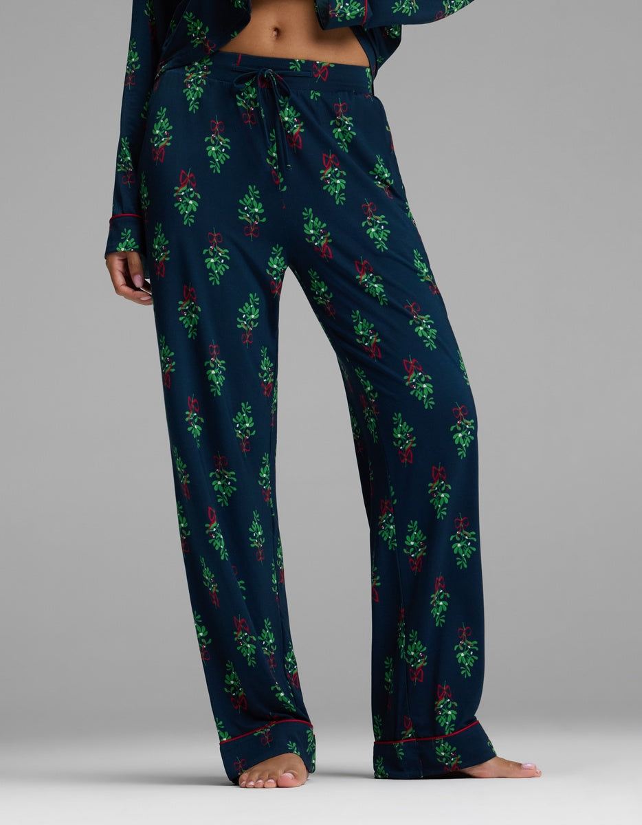 Cozy Earth Women’s Bamboo Stretch-Knit Pajama Pant in navy blue with a repeating pattern of green sprigs and red ribbons, a drawstring waist, and red trim at the cuffs.