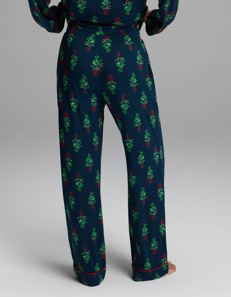 Cozy Earth Women’s Bamboo Stretch-Knit Pajama Pant in navy blue with a repeating pattern of green mistletoe sprigs, red bows, and red piped hems.