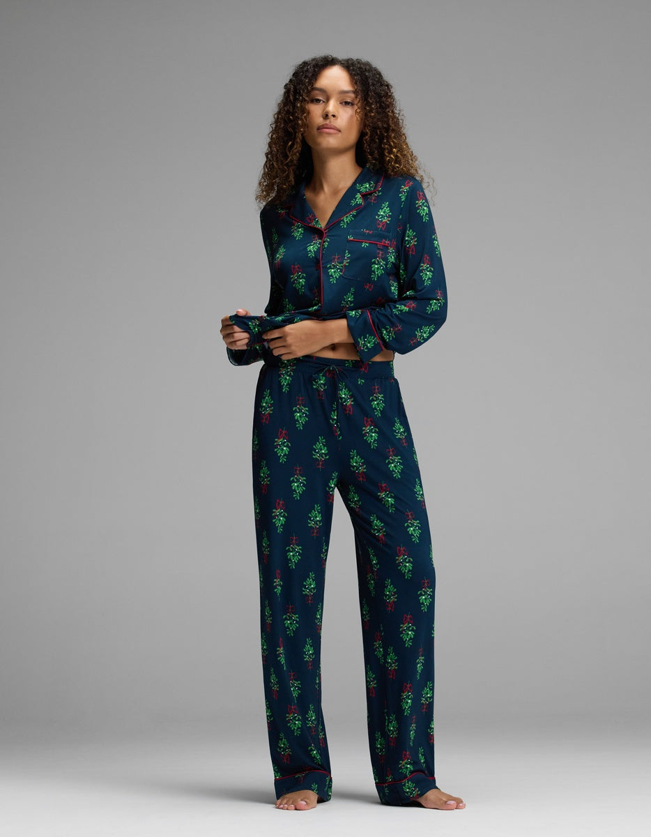 A woman wearing Women’s Bamboo Stretch-Knit Pajama Pant in a dark blue set with a green and red mistletoe print and red piping.