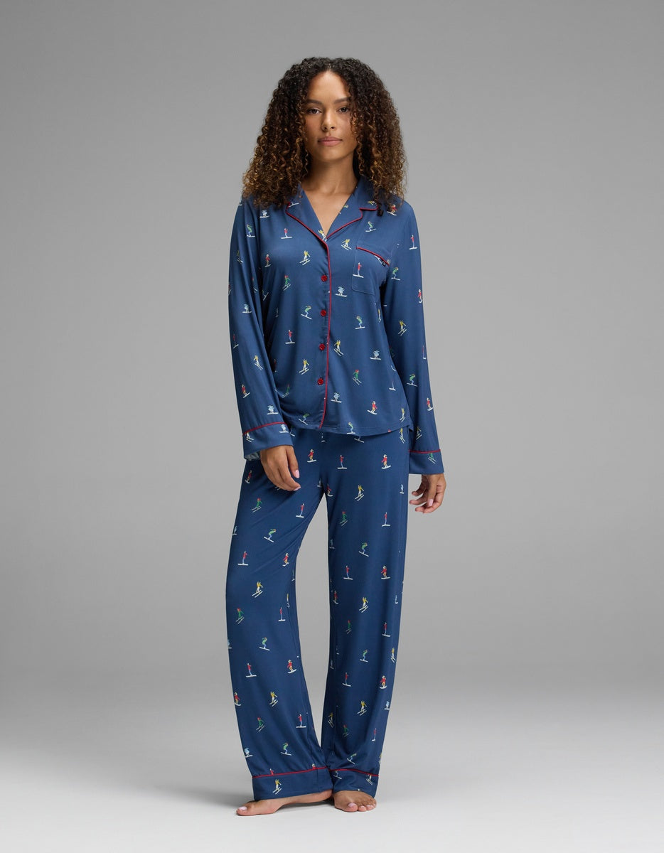 A woman wearing Cozy Earth Women’s Bamboo Stretch-Knit Pajama Pant in navy blue with a small skiing figure pattern and red piping trim.