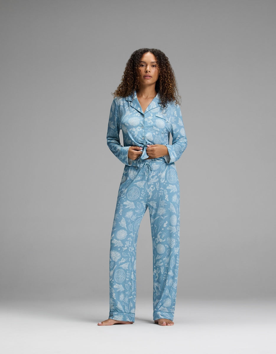 A person wearing a blue button-down pajama top and matching Women’s Bamboo Stretch-Knit Pajama Pant with a white botanical print.
