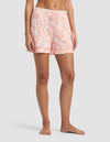 A person stands barefoot, shown from mid-torso to feet against a plain background, wearing Cozy Earth Women's Bamboo Stretch-Knit Pajama Shorts in a peach and white floral pattern with a drawstring waist and relaxed fit.|Color:Melon Toile