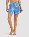 A person wears Cozy Earth Women's Bamboo Stretch-Knit Pajama Shorts in blue with a white floral pattern, standing barefoot against a plain background.|Color:Garden Toile in Sailor