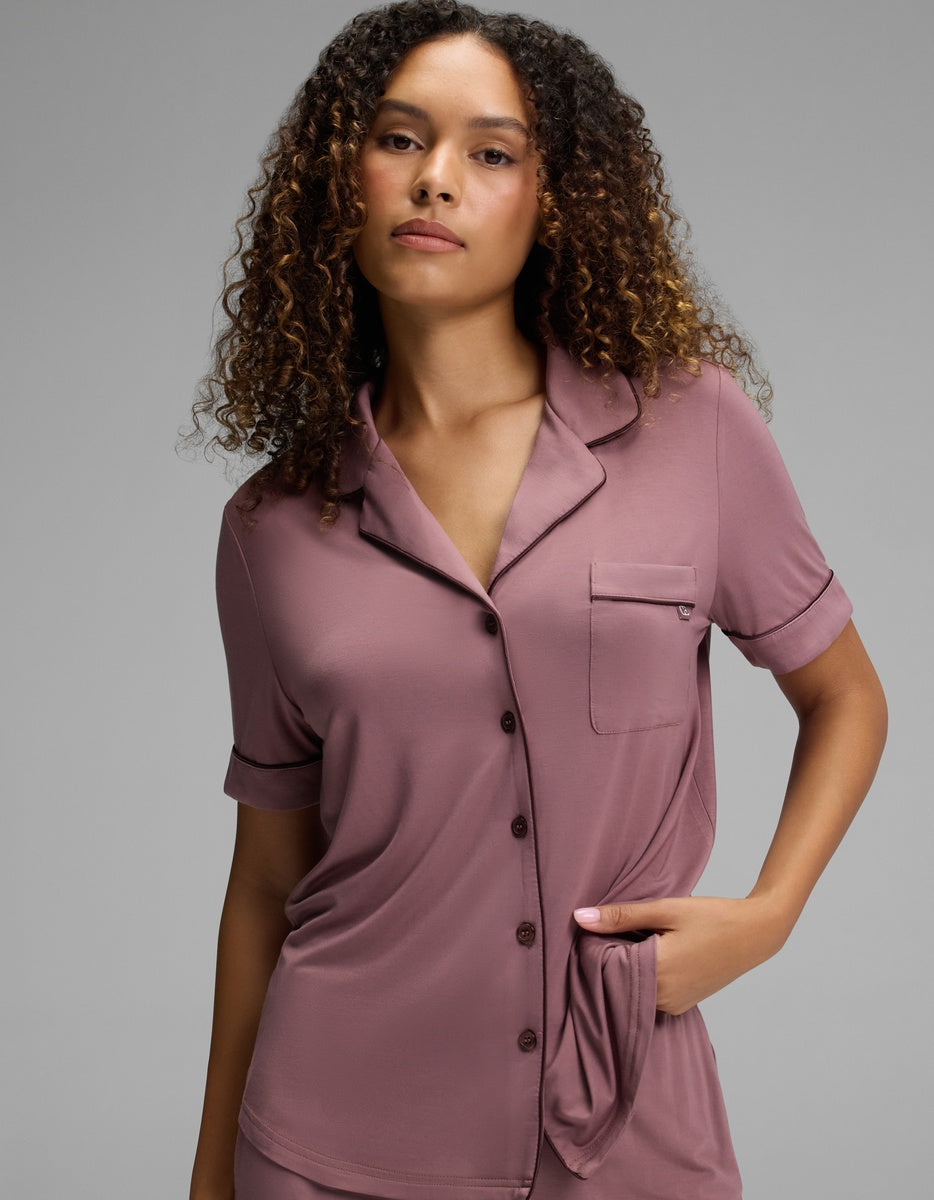 A person wears a dusty rose Women’s Bamboo Stretch-Knit Short Sleeve Pajama Top, featuring a button-down front, collar, and chest pocket.