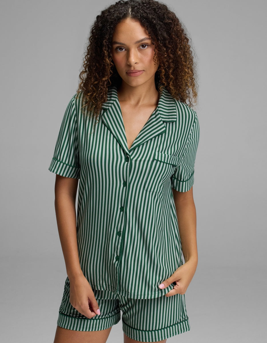 A person wearing a green and white vertical striped, short-sleeve Cozy Earth Women’s Bamboo Stretch-Knit Short Sleeve Pajama Top with a notched collar and a chest pocket.