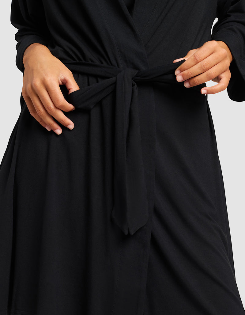 A person adjusts the waist tie of a Cozy Earth Women's Bamboo Stretch-Knit Kimono Robe, showing only their torso and hands against a plain background.