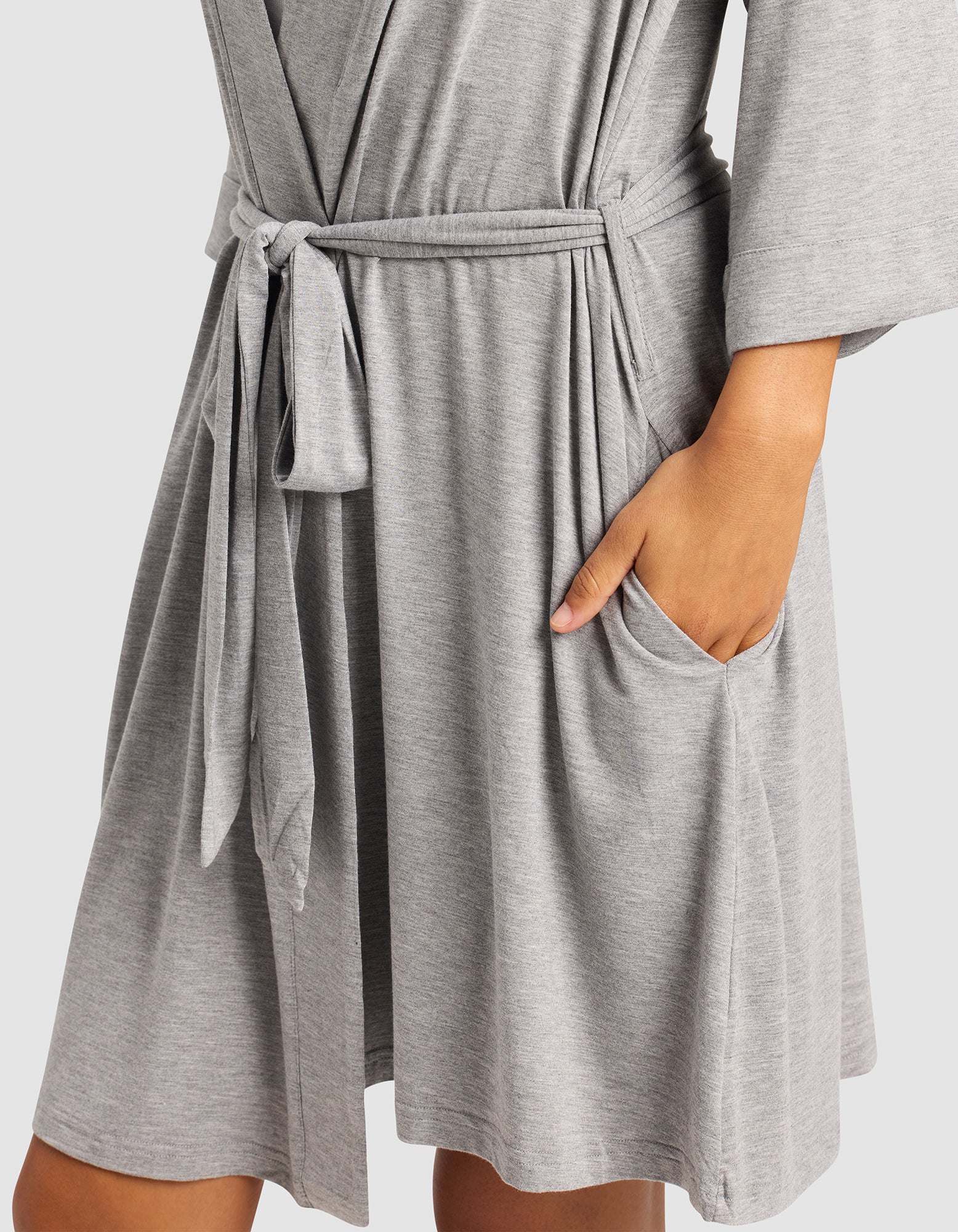 A person wears Cozy Earth's Women's Bamboo Stretch-Knit Kimono Robe in light gray, featuring long sleeves, a relaxed fit, knee length, fabric belt at the waist, and pockets with their right hand tucked in.