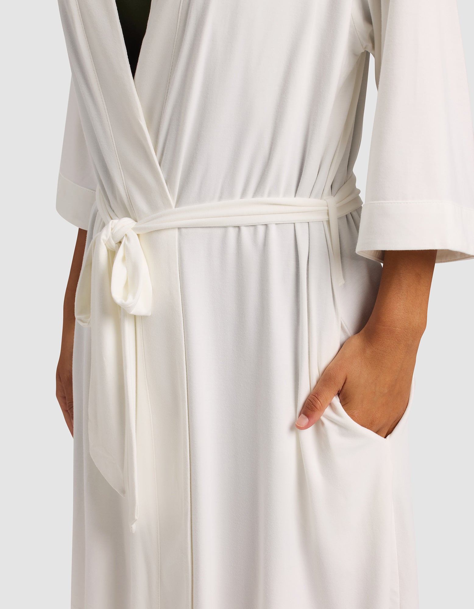 A woman models the Cozy Earth Women's Bamboo Stretch-Knit Kimono Robe—white, tied at the waist with a sash, one hand in a pocket and the other relaxed—against a plain, light background.