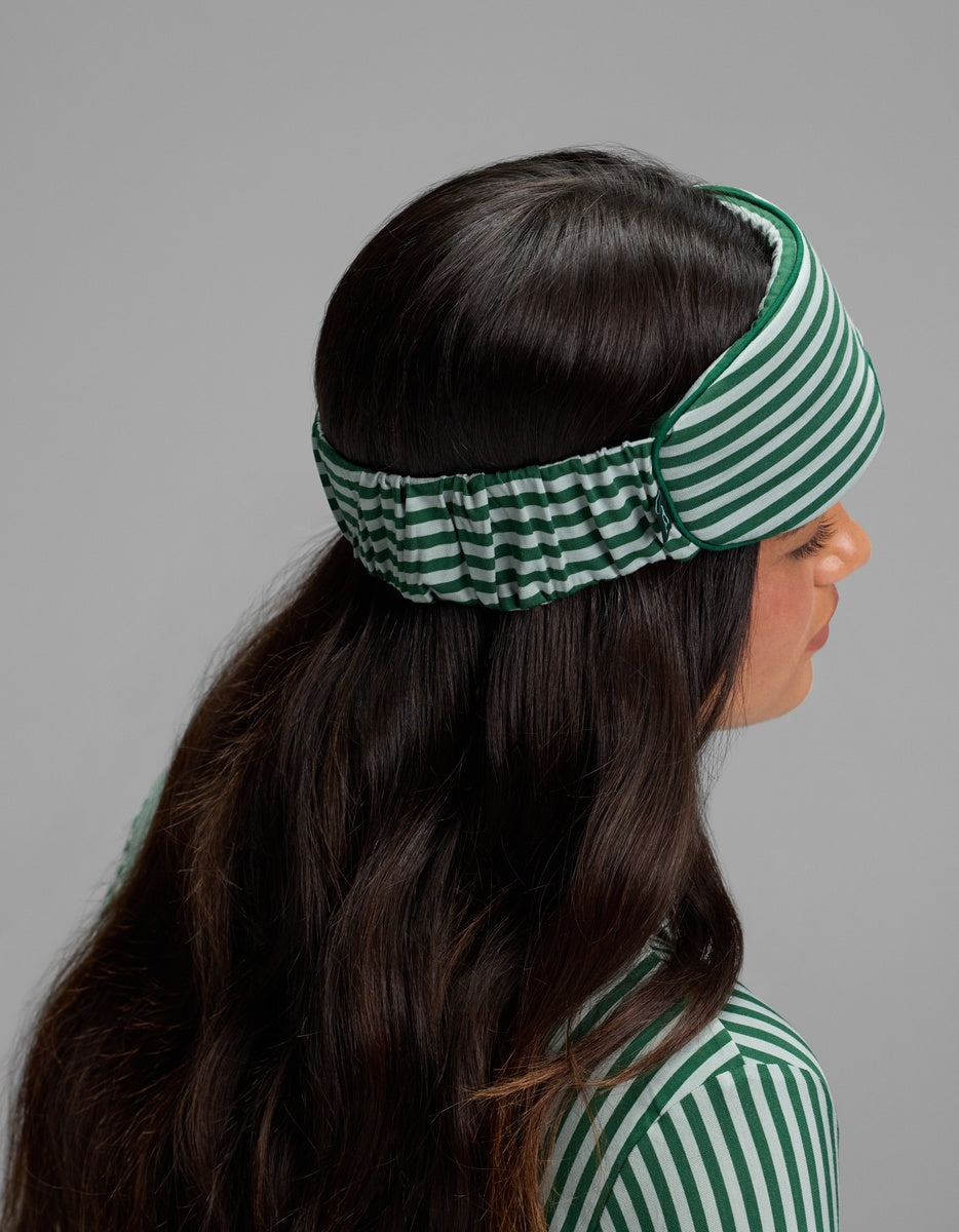 A person wearing a green and white striped Bamboo Stretch-Knit Sleep Mask over their eyes.