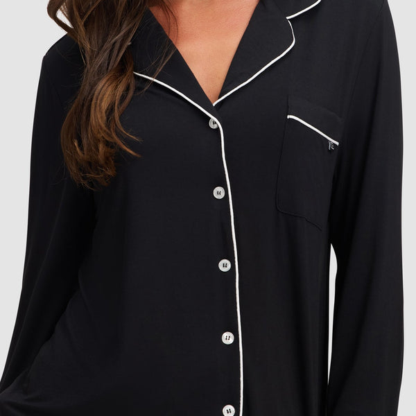 Black pajama top with white piping worn by a model on a plain background