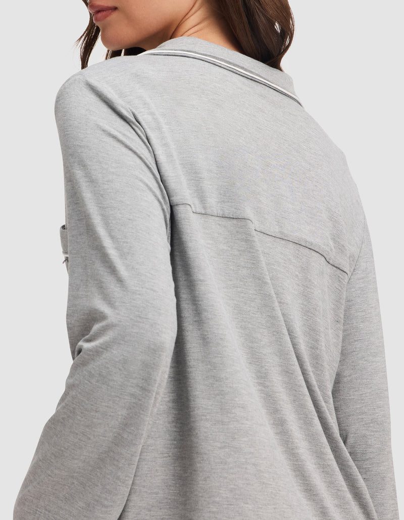 A woman with long brown hair is shown from the side and back, wearing the HIDE Women's Bamboo Stretch-Knit Long Sleeve Pajama Top in light gray. Her face is partially visible against a plain white background.