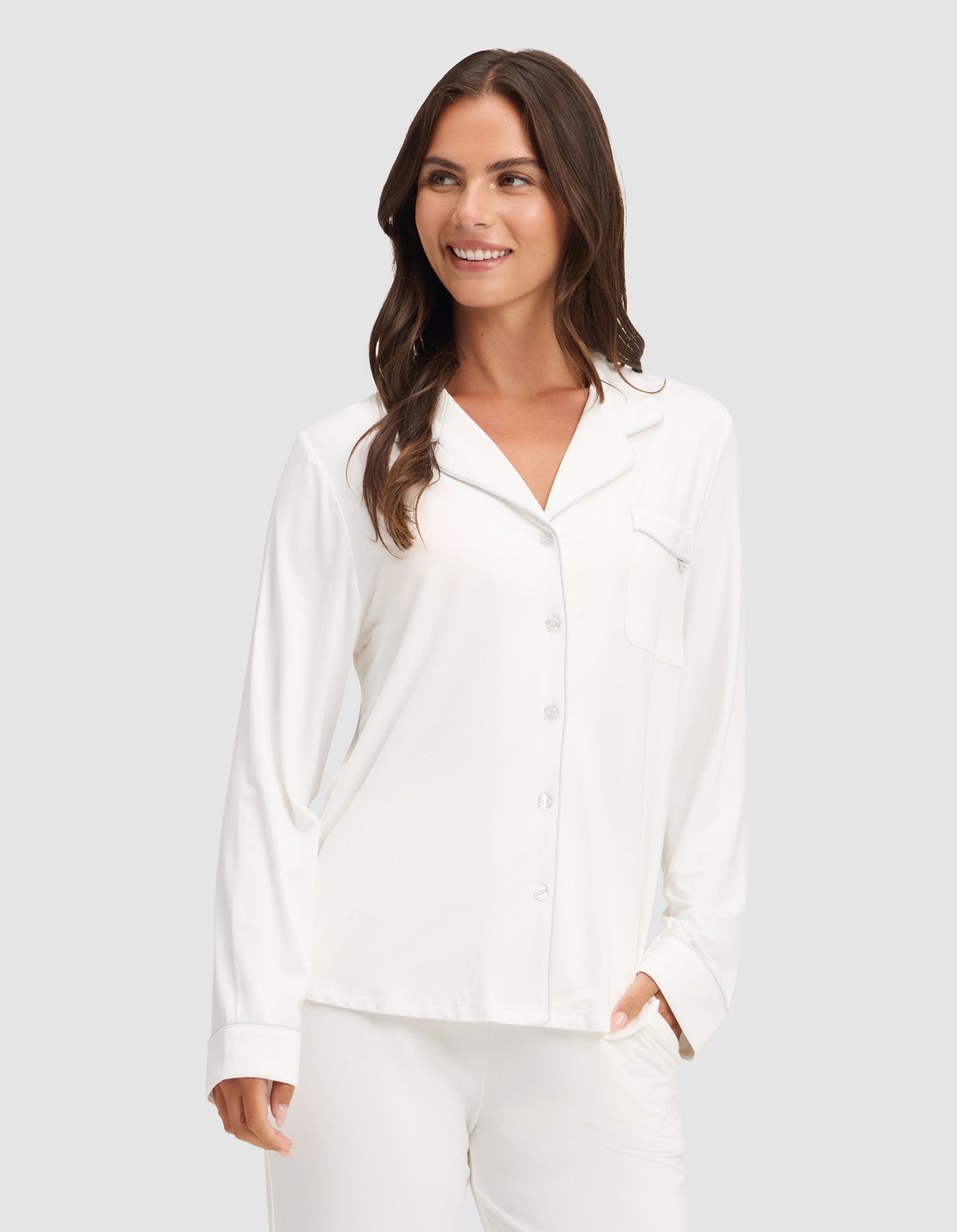A woman smiles against a light gray background wearing HIDE's Women's Bamboo Stretch-Knit Long Sleeve Pajama Top with matching pants. 
