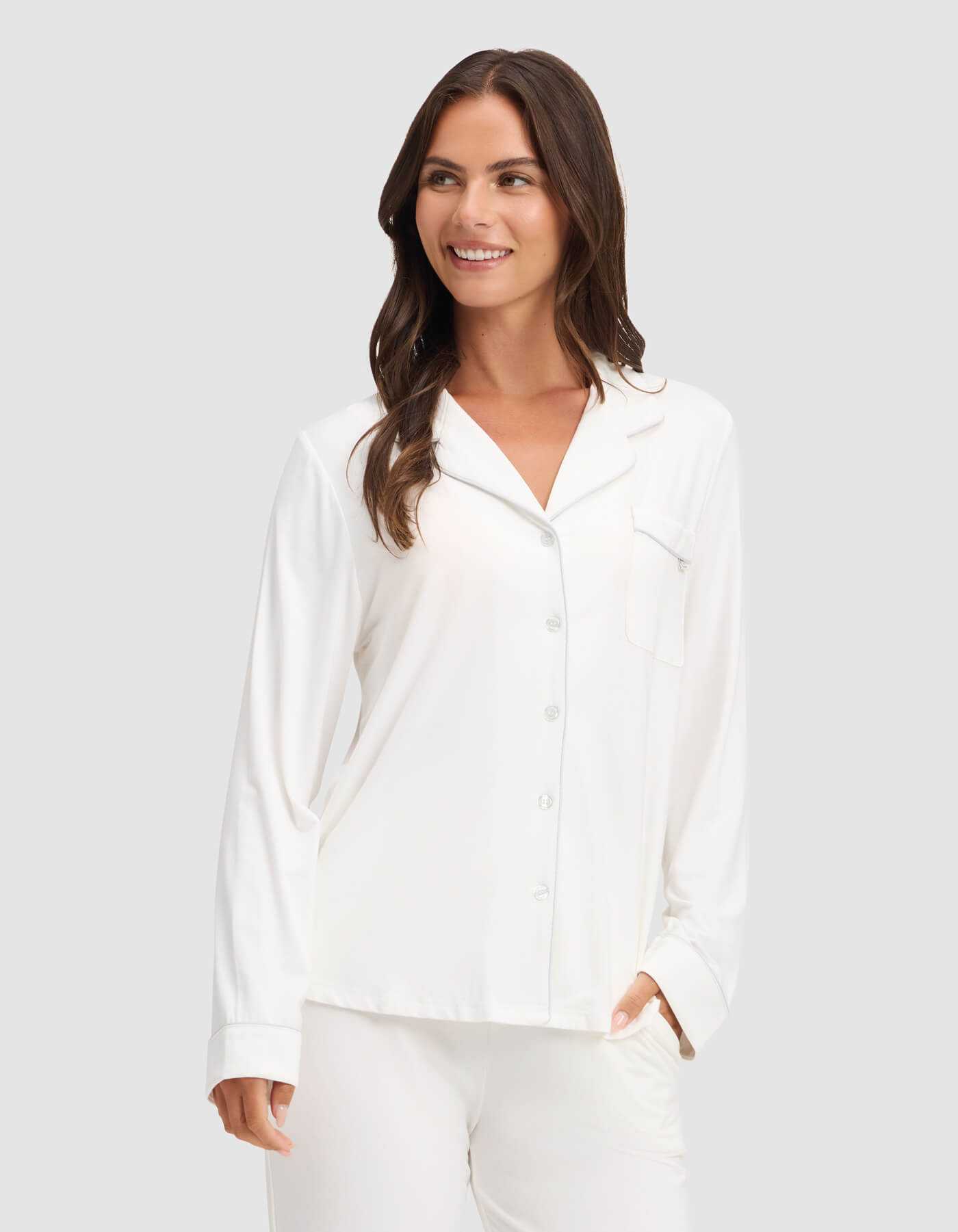 A woman wearing the Cozy Earth Women's Bamboo Stretch-Knit Long Sleeve Pajama Top is smiling while standing against a plain light gray background.