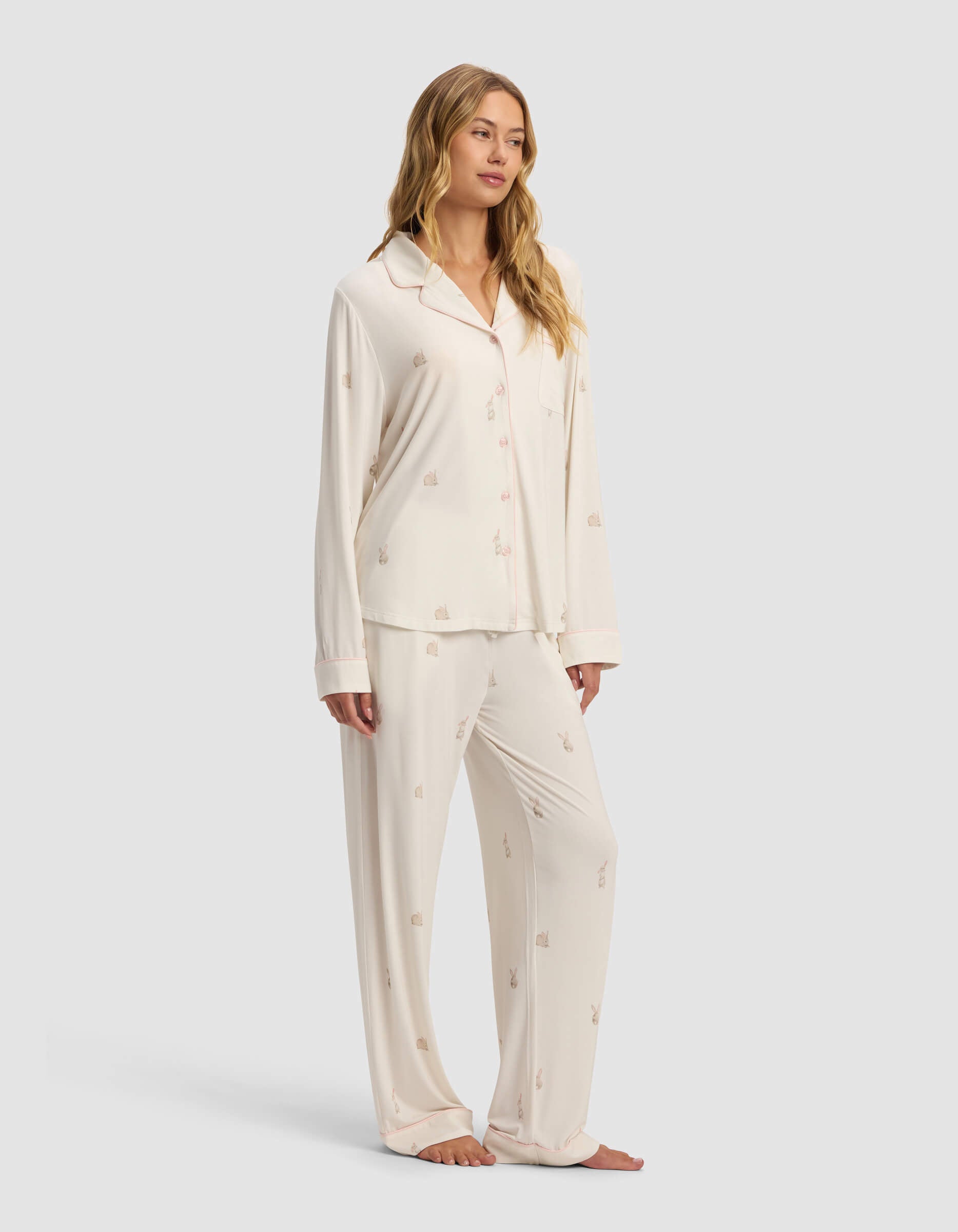 A woman stands barefoot in Cozy Earth's Women's Bamboo Stretch-Knit Long Sleeve Pajama Set, featuring a cream-colored button-up top and loose pants with a subtle small print pattern.|Color:Easter