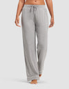 A woman wears Cozy Earth Women's Bamboo Stretch-Knit Pajama Pants in light gray, featuring a drawstring waist and white trim at the cuffs, standing barefoot against a plain background.|Color:Grey