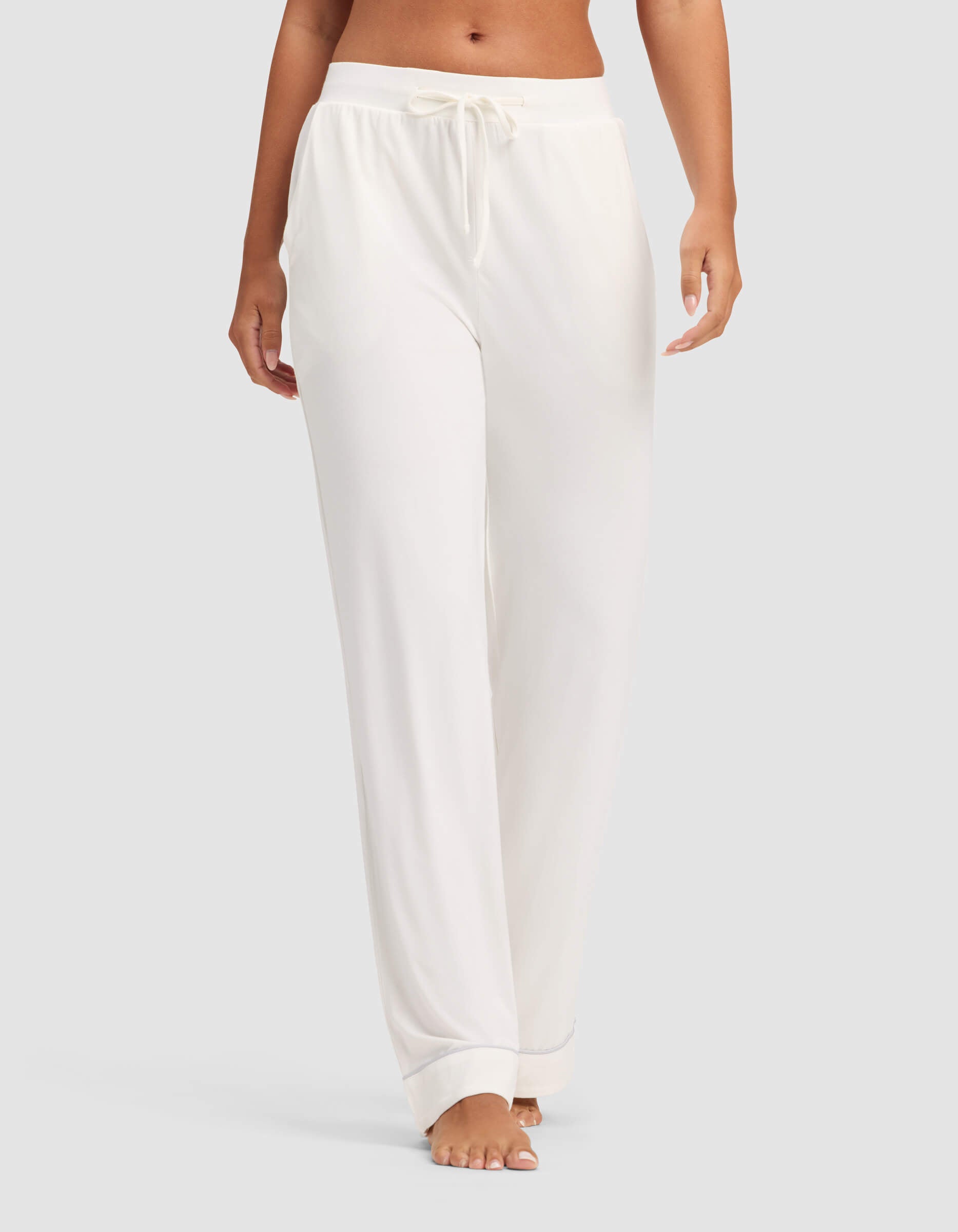 A woman models Cozy Earth's Women's Bamboo Stretch-Knit Pajama Pant, featuring a loose fit and drawstring waist, shown barefoot against a plain light background with only her lower torso and legs visible.
