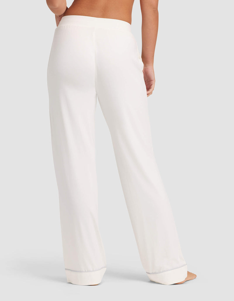 A person stands barefoot, facing away, wearing Cozy Earth Women's Bamboo Stretch-Knit Pajama Pant in white against a plain light gray background.