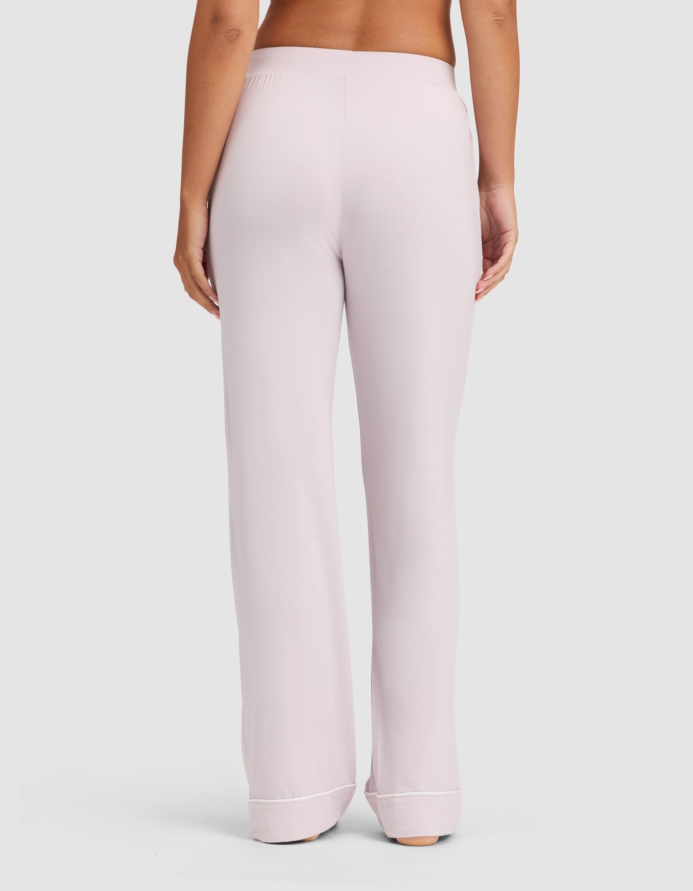 A person is shown from the waist down, barefoot against a plain light background, wearing HIDE Women's Bamboo Stretch-Knit Pajama Pant in light purple with an elastic waistband and cuffed hems. 