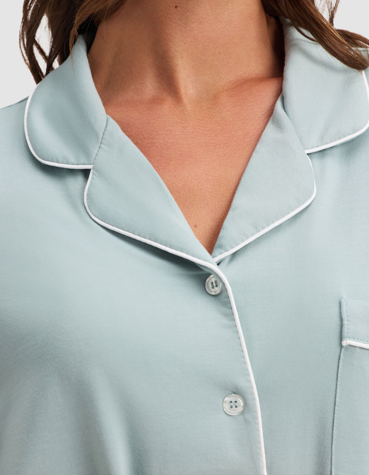 A close-up of a woman wearing the Cozy Earth Women's Bamboo Stretch-Knit Long Sleeve Pajama Top in light blue, featuring white piping, a collar, buttons, and part of the chest pocket.