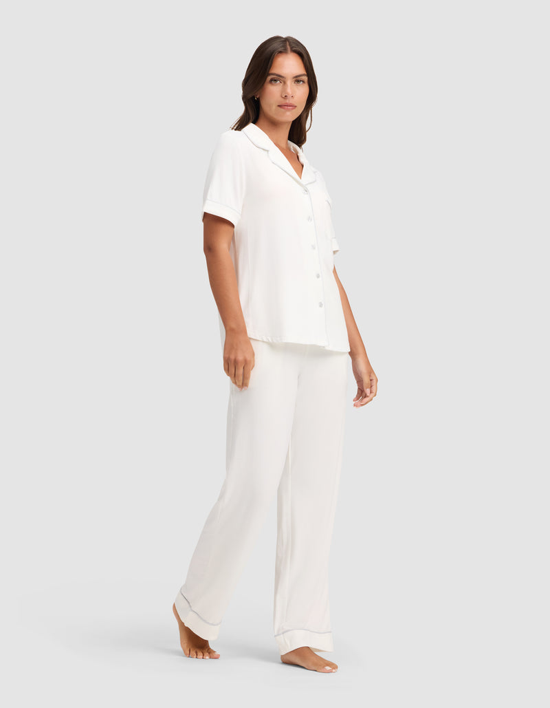 A woman stands barefoot against a plain background, wearing the Cozy Earth Women's Bamboo Stretch-Knit Short Sleeve & Pant Pajama Set.
