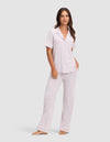 A woman with long hair and a relaxed expression stands barefoot against a plain background, wearing the Cozy Earth Women's Bamboo Stretch-Knit Short Sleeve & Pant Pajama Set in light purple. |Color:Lilac