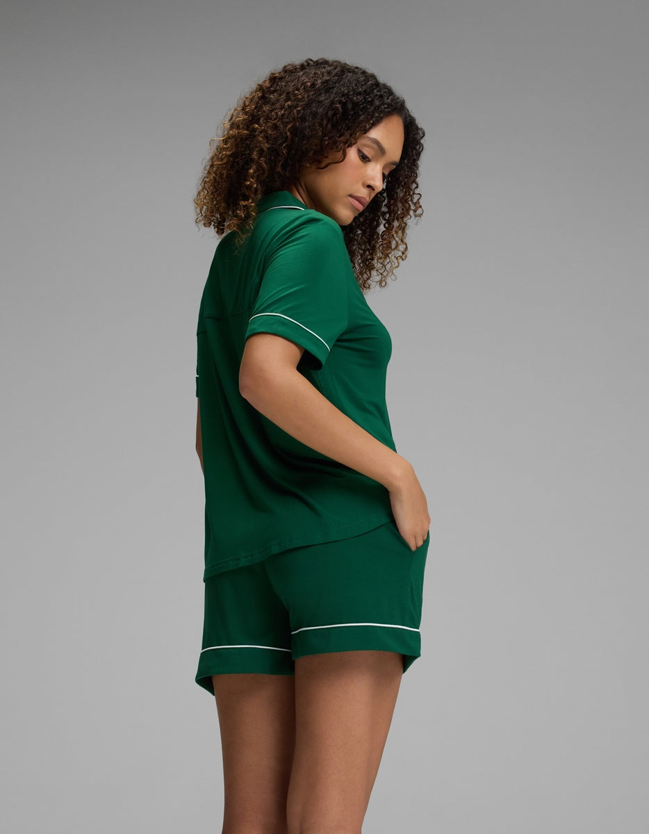 A woman wearing a deep green Cozy Earth Women’s Bamboo Stretch-Knit Short Sleeve Pajama Set with white piping trim.