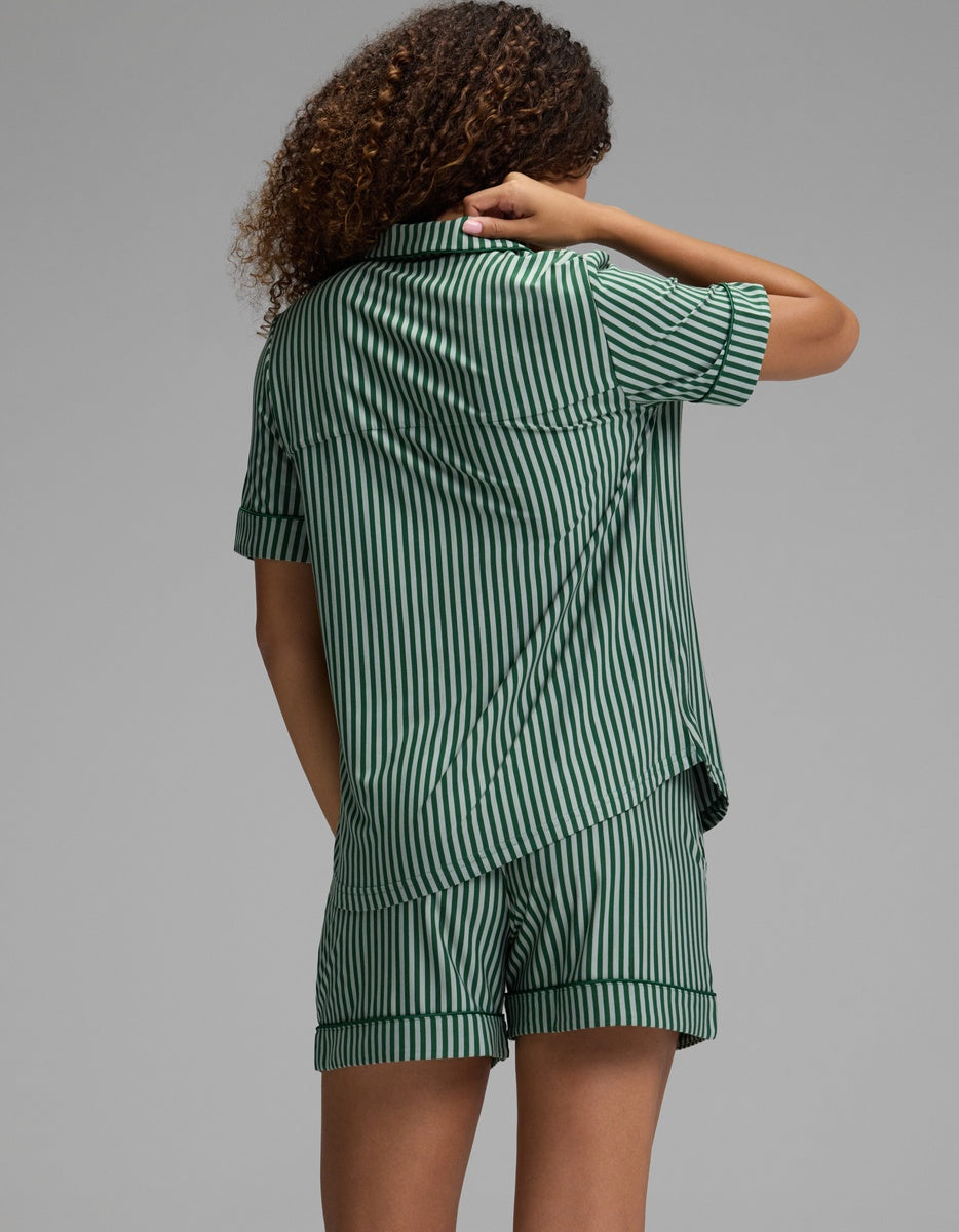A person seen from behind wears a green and white vertical stripe Women’s Bamboo Stretch-Knit Short Sleeve Pajama Set, consisting of a short-sleeved button-up top and matching shorts.