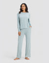 A woman stands barefoot against a plain background, wearing the Cozy Earth Women's Bamboo Stretch-Knit Long Sleeve Lounge Tee & Pant Set in Brook, with one hand in her pocket and a relaxed expression.|Color:Brook