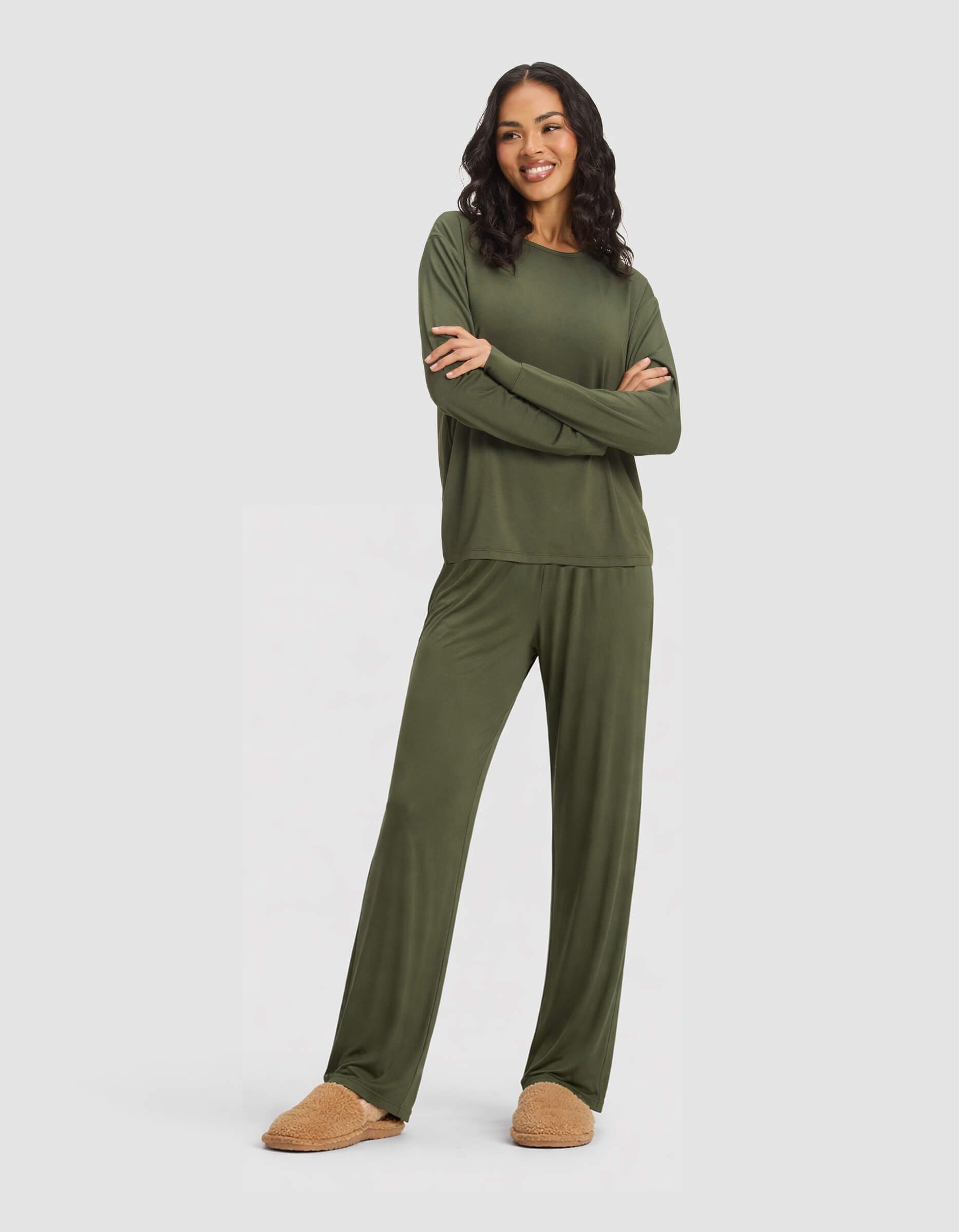 A woman in a Cozy Earth Women's Bamboo Stretch-Knit Long Sleeve Lounge Tee & Pant Set, Olive, stands against a light background with her arms crossed and smiling.