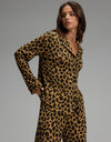 A woman stands against a plain gray background, looking to the side with her hands in her pockets while wearing the Cozy Earth Women’s Bamboo Stretch-Knit Long Sleeve Pajama Top in a matching leopard print set.|Color:Leopard Print in Onyx