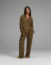 A woman stands barefoot against a plain grey background, wearing the Cozy Earth Women’s Bamboo Stretch-Knit Long Sleeve Pajama Set featuring a matching brown and black leopard print.|Color:Leopard Print in Onyx