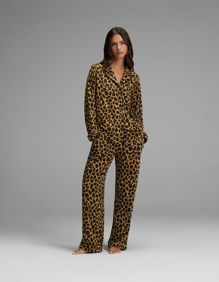 A woman stands barefoot against a plain grey background, wearing the Cozy Earth Women’s Bamboo Stretch-Knit Long Sleeve Pajama Set featuring a matching brown and black leopard print.