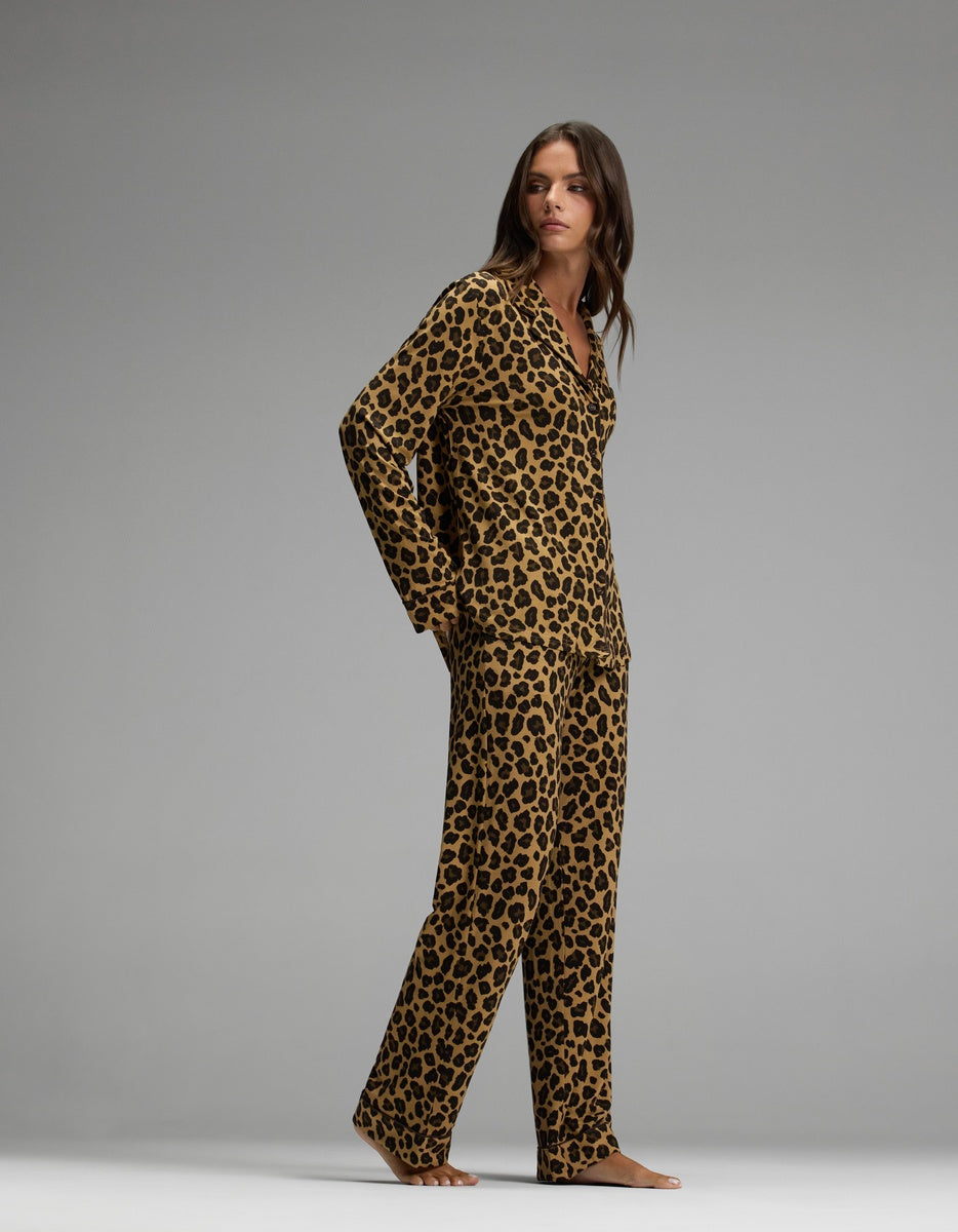 A woman stands barefoot, facing slightly to the side against a plain gray background, wearing the Cozy Earth Women’s Bamboo Stretch-Knit Long Sleeve Pajama Set in a matching leopard print.