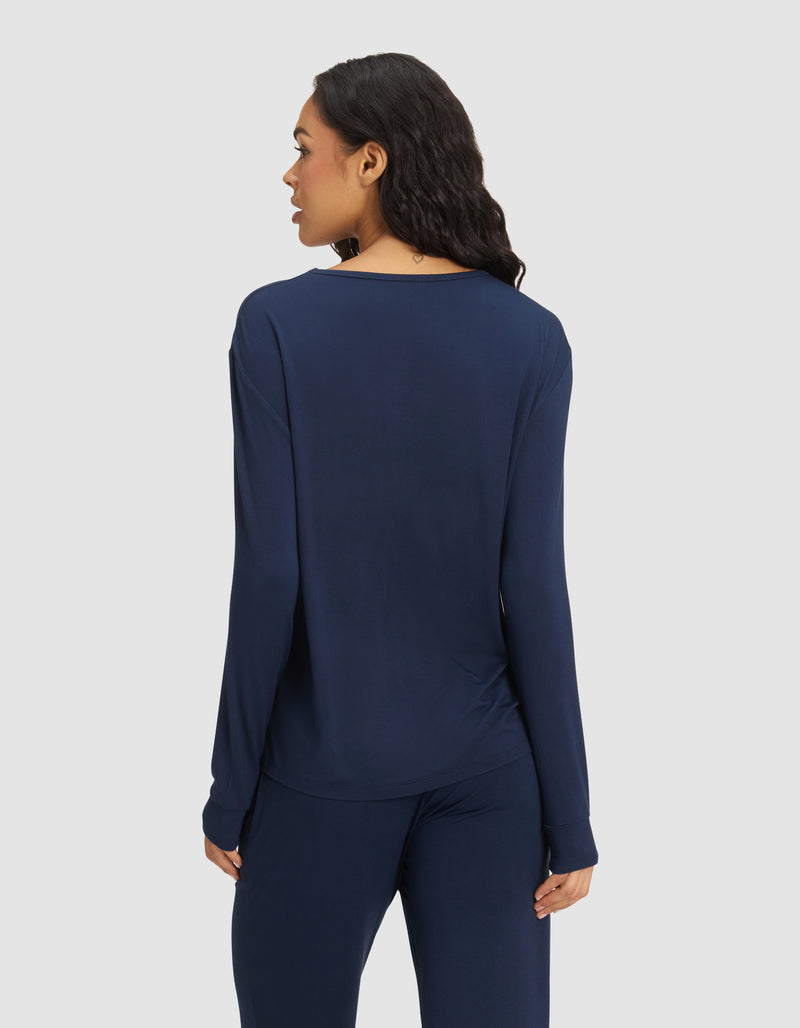 A woman with long dark hair is seen from the back, wearing the Cozy Earth Women's Bamboo Stretch-Knit Long Sleeve Lounge Tee in navy blue, standing against a plain light background.
