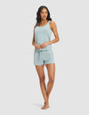 A woman stands barefoot in the Cozy Earth Women's Bamboo Stretch-Knit Tank & Short Set, featuring a light blue sleeveless top and matching drawstring shorts, against a plain white background.|Color:Brook