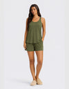 A woman faces forward in the Cozy Earth Women's Bamboo Stretch-Knit Tank & Short Set in olive green, paired with beige slippers. She has long straight hair, a neutral expression, and stands against a plain light background.|Color:Olive
