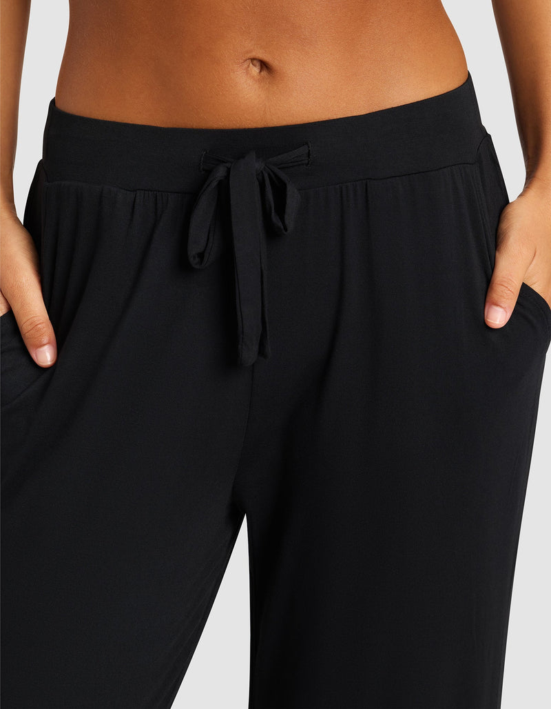 A close-up shows a person wearing Cozy Earth's Women's Bamboo Stretch-Knit Pant, hands in the pockets, highlighting the waistband and midriff against a plain background.