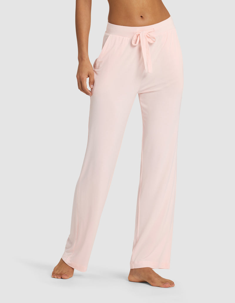 A woman wears Cozy Earth Women's Bamboo Stretch-Knit Pant in light pink, featuring a loose fit, elastic waistband, and drawstring, standing barefoot against a plain background.