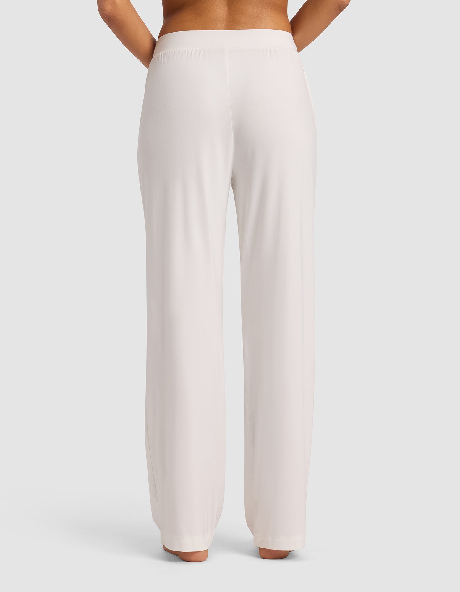 A person stands facing away, wearing Cozy Earth's Women's Bamboo Stretch-Knit Pant in light beige. The high-waisted pants feature a smooth, relaxed fit with no visible pockets or patterns, set against a plain light background.