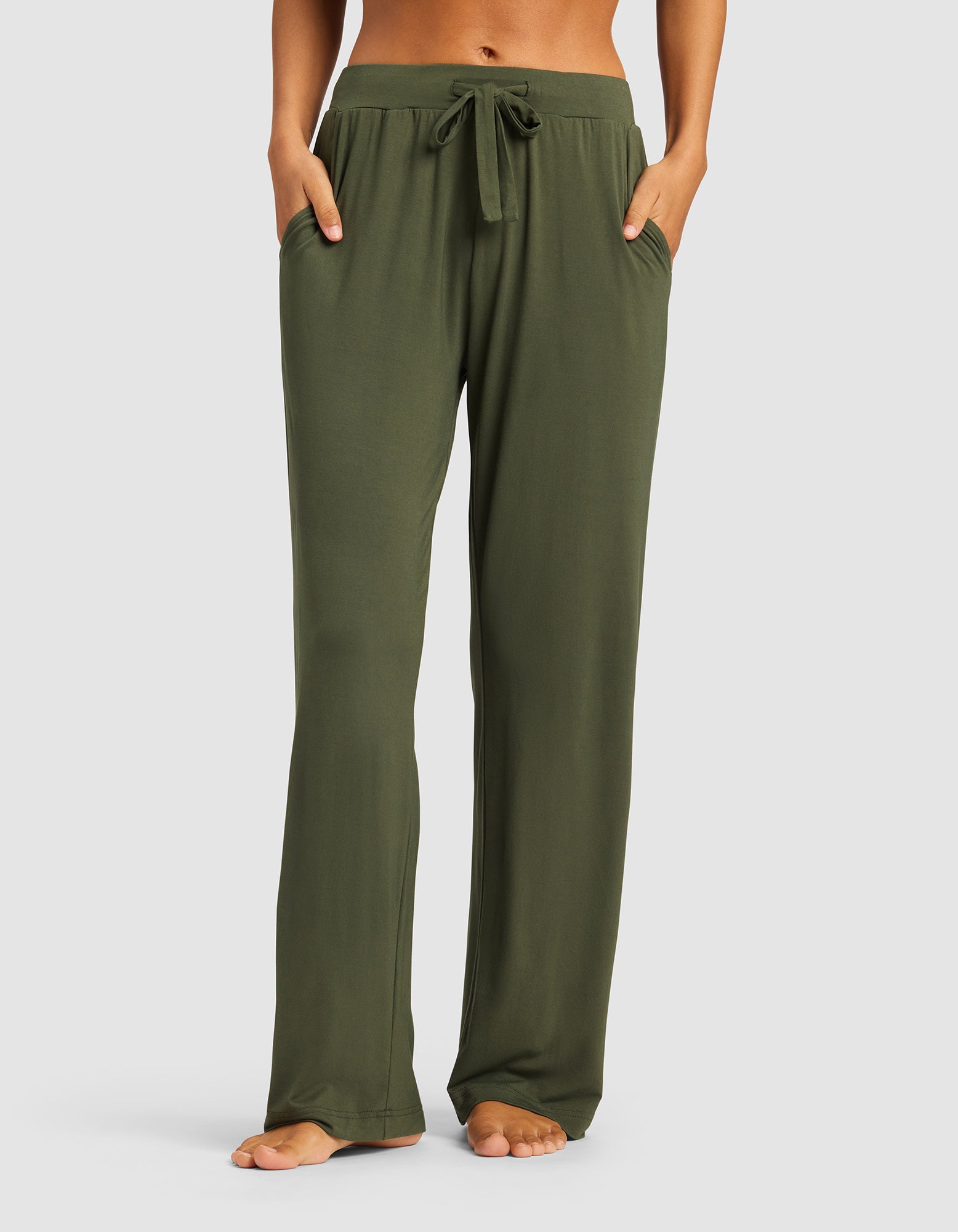 A person wears Cozy Earth's Women's Bamboo Stretch-Knit Pant in olive green, featuring a relaxed fit, drawstring waist, and full length. Hands are in the pockets, they're barefoot, and the upper body is not visible.