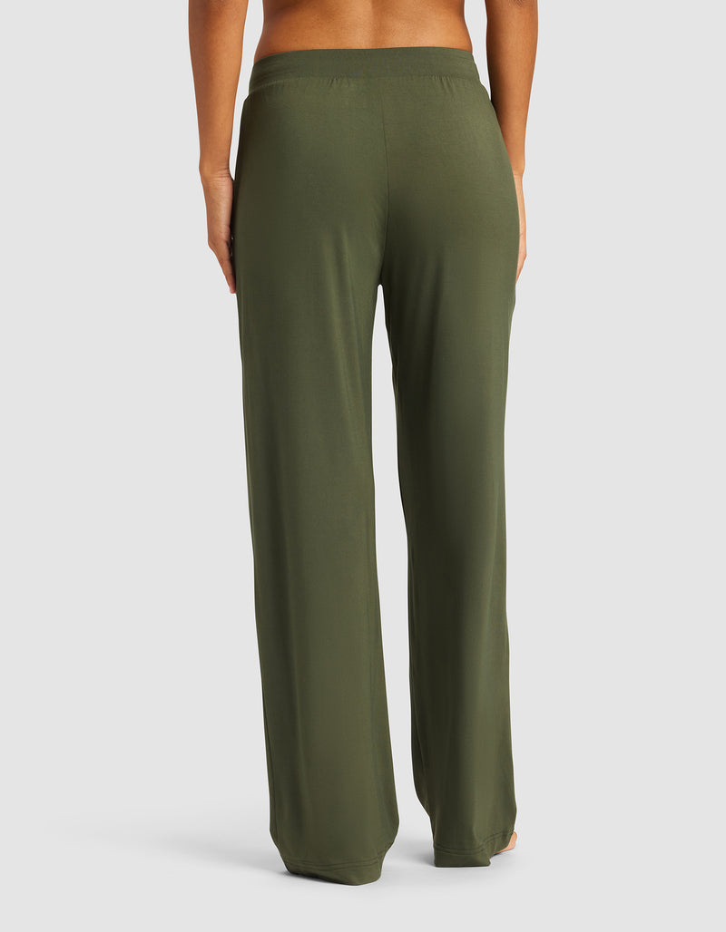 A woman is pictured from the waist down, barefoot against a plain light background, wearing Cozy Earth Women's Bamboo Stretch-Knit Pant in olive green with a relaxed fit.