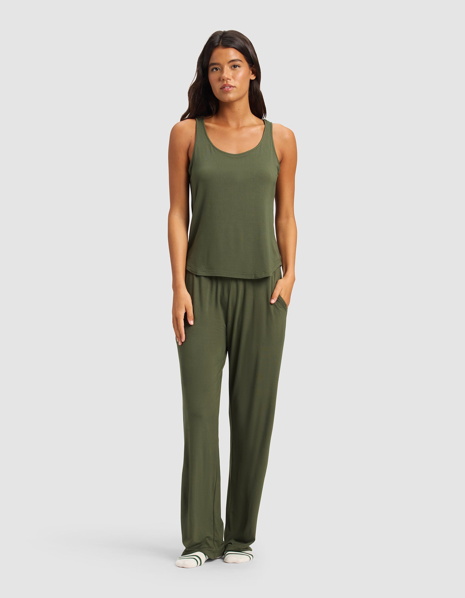 A woman faces forward wearing Cozy Earth’s Women's Bamboo Stretch-Knit Pant in olive green with a matching sleeveless tank top and white slide sandals, standing against a plain light gray background.|Color:Olive