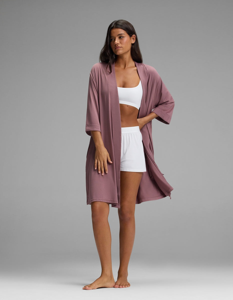 A person wears a mauve, open-front Women’s Bamboo Stretch-Knit Kimono Robe over a white bralette and shorts.
