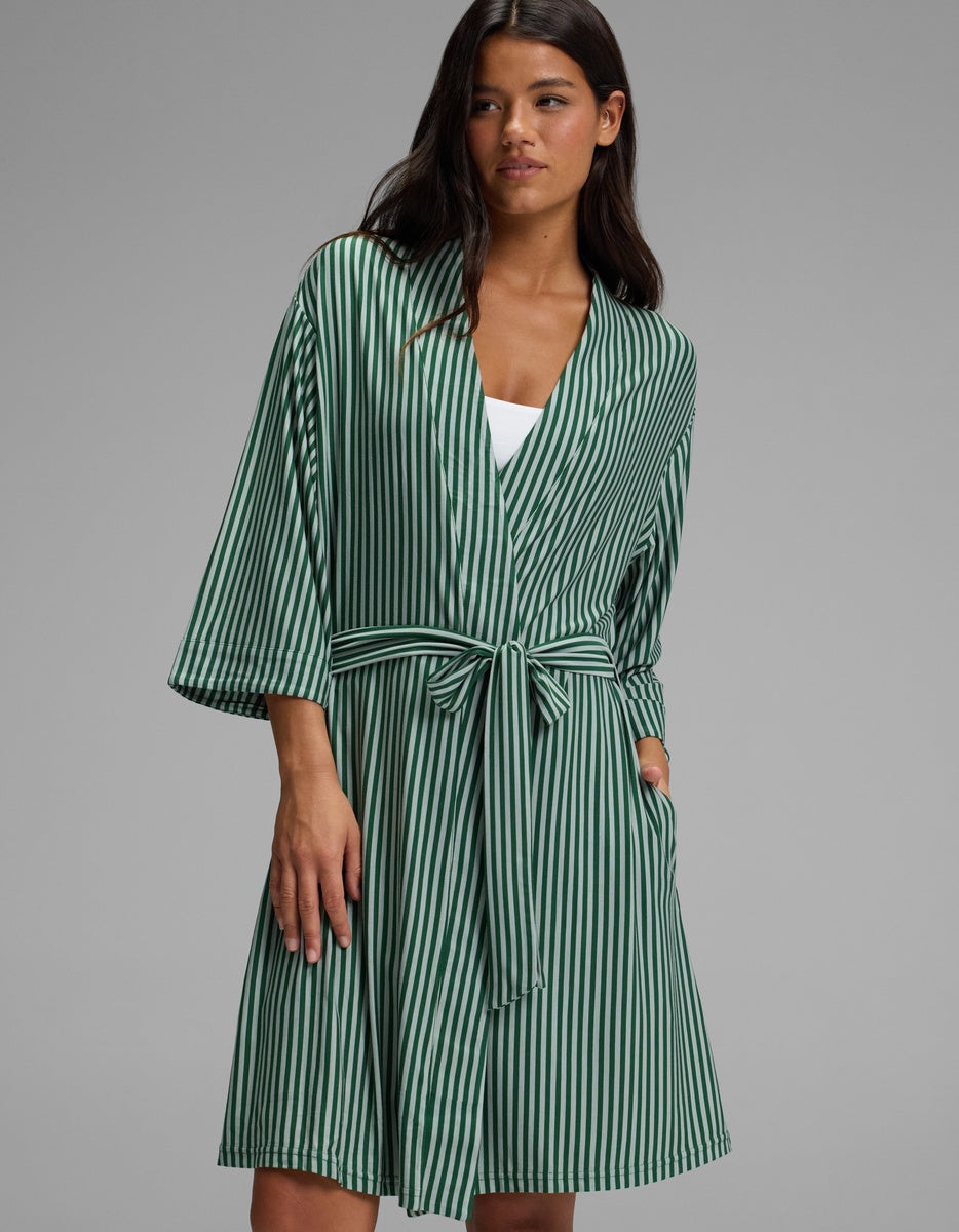 A woman wearing a knee-length, green and white striped Cozy Earth Women’s Bamboo Stretch-Knit Kimono Robe with a tie waist.